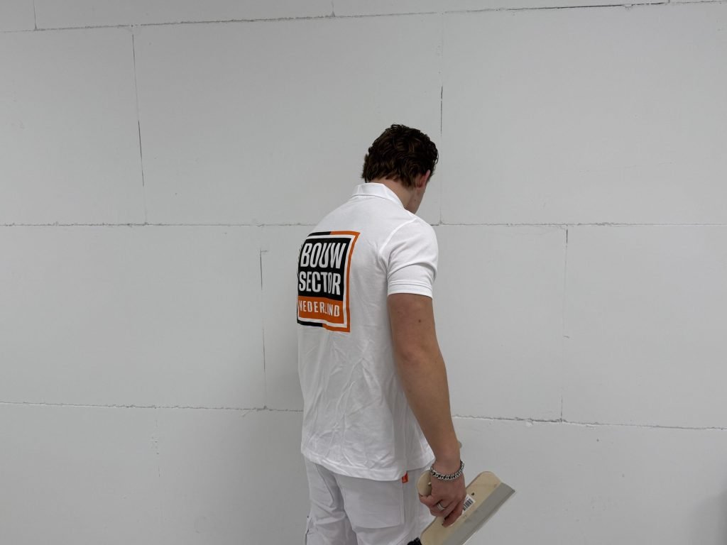 Stukadoor van Bouwsector Nederland bekijkt met een spaan in de hand een wand met zichtbare naden