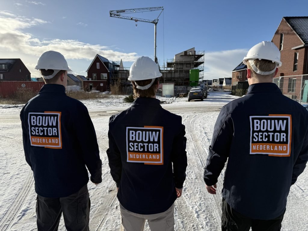 Drie vakmensen in werkjassen met het logo van Bouwsector Nederland kijken naar woningen in aanbouw